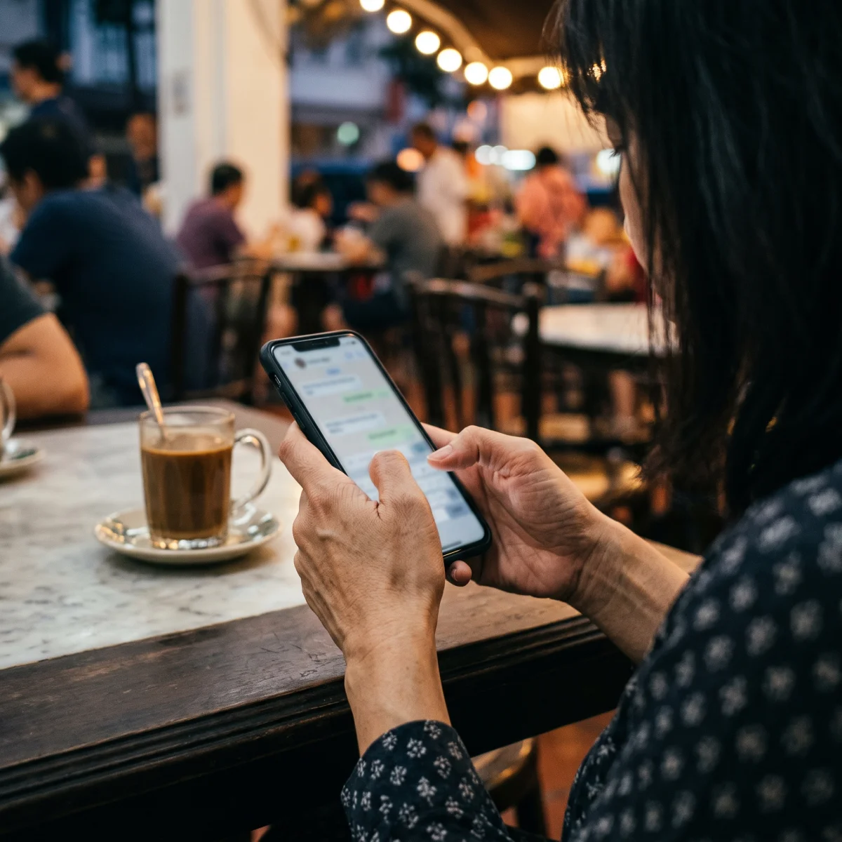 Close-up of hands replying to a message on a phone at a kopitiam table